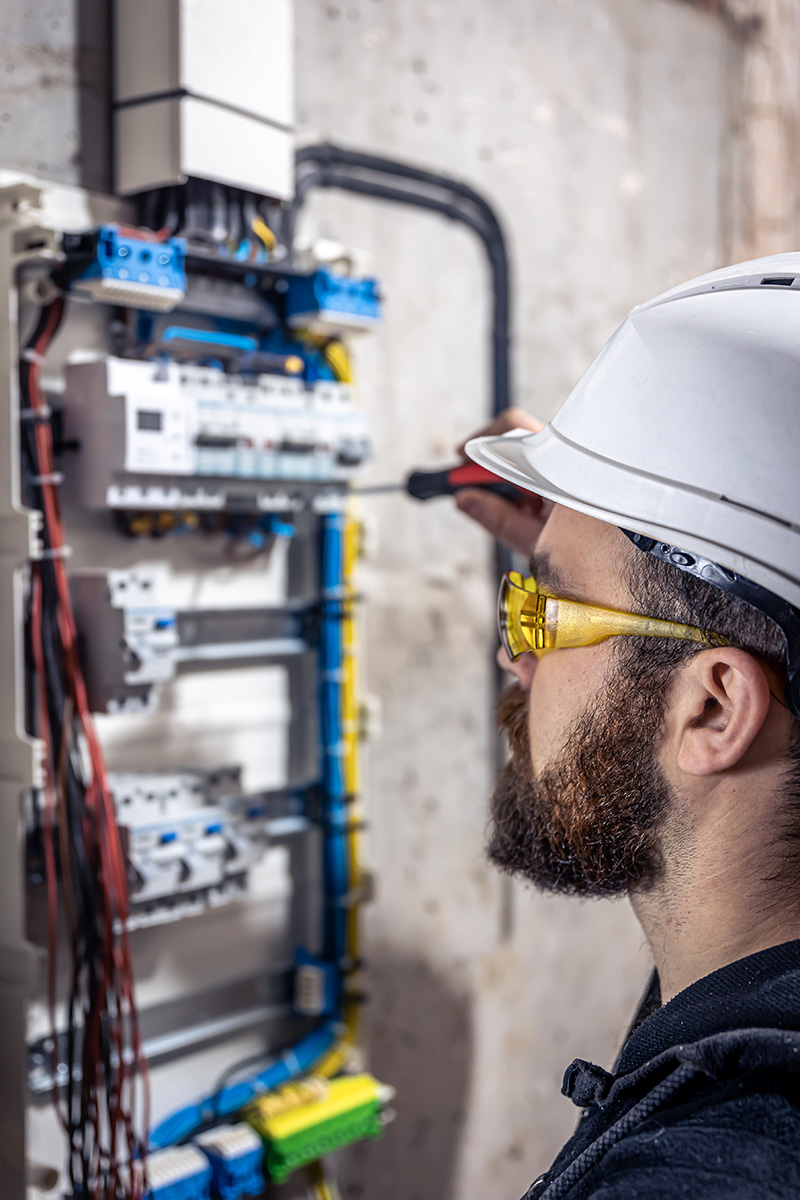 A male electrician works in a switchboard with an electrical connecting cable.